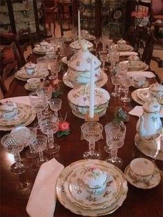 a dining room table set with china dishes and candlesticks, plates and napkins