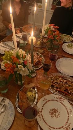 a group of people sitting around a table with food and candles in the middle of it