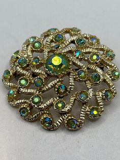 Vintage Aurora Borealis stone brooch on gold tone metal with a roll over clasp Gold Jeweled Brooches For Formal Occasions, Formal Gold Jeweled Brooches, Ornate Jeweled Gold Brooches, Green Round Brooch For Formal Occasions, Ornate Gold Jeweled Brooches, Gold Round Brooch Pins, Gold Jeweled Brooches For Party, Gold Jeweled Costume Jewelry Brooch, Gold Clip-on Costume Jewelry Brooch