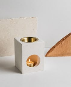 a white candle holder with a wooden triangle next to it and a small candle in the middle