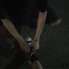 a person tying their shoelaces on top of another persons foot in the dark