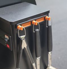 three pairs of scissors are attached to the side of a black box with orange handles