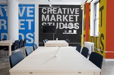 an office space with tables and chairs in front of colorful wallpaper that reads creative market studios