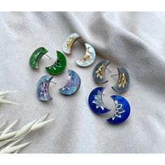 six pairs of earrings sitting on top of a white sheet next to dried flowers and grass