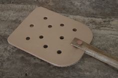 a spatula with holes in it sitting on the ground next to a wooden handle