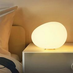 a white light sitting on top of a metal box next to a bed with pillows