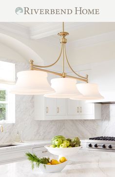 a kitchen with marble counter tops and white cabinets, along with a bowl of fruit on the island