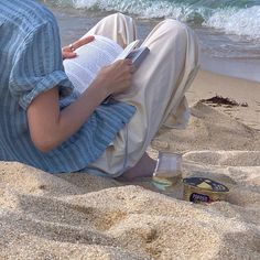 a person sitting in the sand reading a book and drinking some wine on the beach