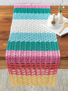 a crocheted table runner on top of a wooden table next to a vase