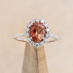 an oval shaped pink diamond surrounded by small white diamonds on top of a wooden stand