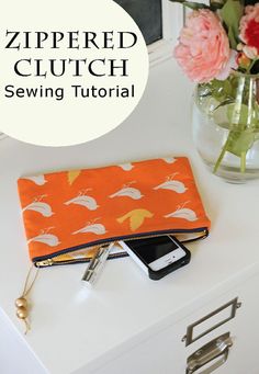 an orange zippered clutch sitting on top of a white table next to a vase with flowers