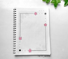 an open notebook with pink flowers on it next to some green leaves and ivys