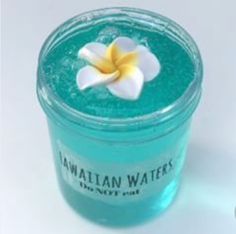 a blue jar with a flower in it sitting on a white table next to a bottle of hawaiian water