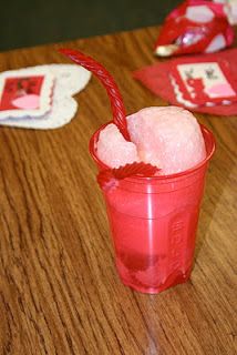 a red cup filled with ice sitting on top of a wooden table next to coasters