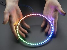 two hands reaching for a circular light with colored lights around it on a dark surface