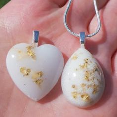 two white heart shaped pendants with gold flecks in the palm of someone's hand