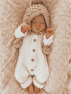 a newborn baby wearing a knitted hat and white sweater laying on top of a blanket