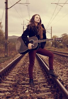 a woman holding a guitar while standing on train tracks