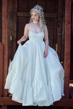 a woman in a white dress is standing on a wooden platform and posing for the camera