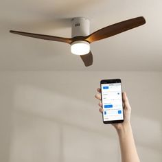 a person holding a cell phone up to a ceiling fan