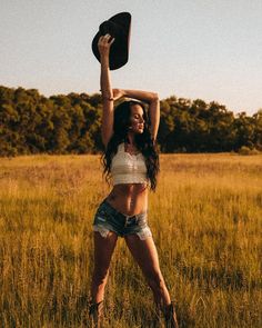 a woman standing in a field with her hat on her head and arms above her head