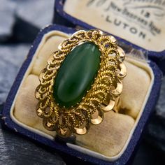 This ornate vintage ring showcases an oval nephrite jade cabochon surrounded by intricately looped, twisted, and scalloped gold detailing. The ring is made of 14k yellow gold and is currently a size 7.5. Vintage Oval Jade Rings, Vintage Gold Emerald Cabochon Ring, Antique Gold Emerald Ring With Oval Cabochon, Antique Oval Cabochon Emerald Ring, Antique Emerald Ring In Gold With Oval Cabochon, Vintage Jade Cabochon Ring, Vintage Jade Rings For Formal Occasions, Vintage Oval Jade Emerald Ring, Victorian Oval Filigree Ring With Cabochon