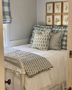 a white bed topped with lots of pillows next to framed pictures on the wall above it