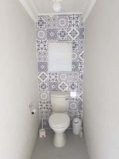 a white toilet sitting inside of a bathroom next to a wall covered in blue and white tiles