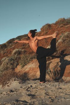 a man standing on one leg in the sand with his arms spread out and legs crossed