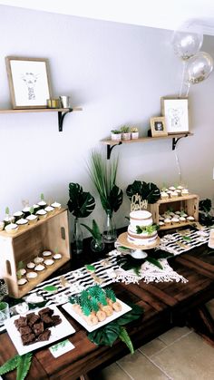 a table topped with cakes and cupcakes on top of wooden tables covered in greenery