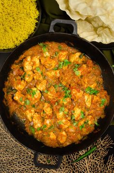 a skillet filled with food next to rice and other foods on a table top