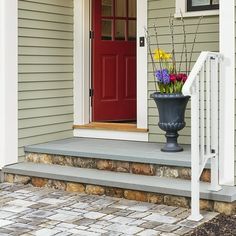 a vase with flowers sitting on the front steps of a house next to a red door