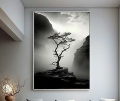 a black and white photo of a lone tree on a cliff in the foggy mountains