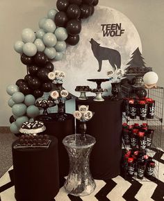 a dessert table with black and white balloons, silver cake stands, and an animal themed backdrop