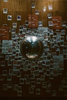 a disco ball is surrounded by many photos and magnets on a wooden wall with a mirror hanging from the ceiling