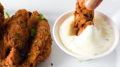 fried chicken is being dipped with ranch dressing in a white bowl next to a dipping sauce