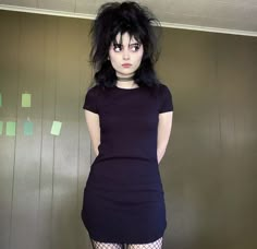 a woman with black hair and tights standing in front of a wall wearing fishnet stockings