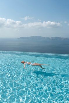 a woman swimming in a pool with clear blue water and an island in the distance