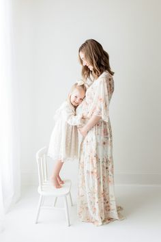 a mother and her daughter standing in front of a white chair with their arms around each other