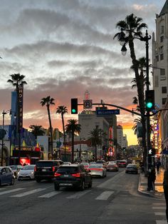 cars are stopped at an intersection with palm trees in the foreground and people walking on the sidewalk