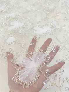 a person's hand is covered with beads and pearls on a white fabric background