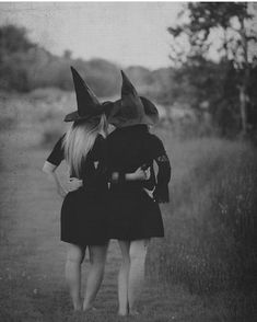 two women wearing witches hats walking down a dirt road in black and white, back to back