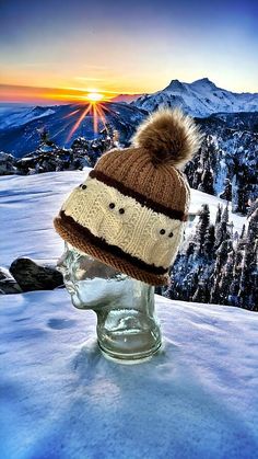 a knitted hat sitting on top of a head in the snow with mountains in the background