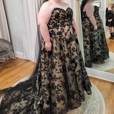 a woman is standing in front of a mirror wearing a black dress with flowers on it