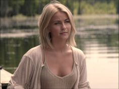 a woman standing in front of a body of water with her eyes closed and looking off to the side