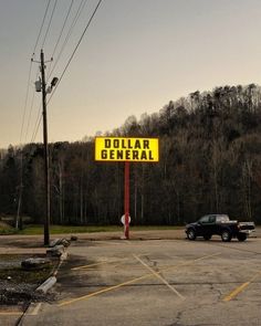 a yellow dollar general sign sitting in the middle of a parking lot next to a forest