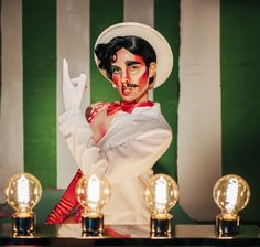 a woman with makeup on holding her hand up in front of some lights and a green striped wall