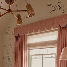 a bedroom with pink curtains and floral wallpaper on the walls next to a window