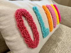 a close up of a pillow on a couch with crocheted letters in the middle