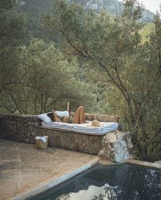 a woman laying on top of a bed next to a pool in a forest filled with trees